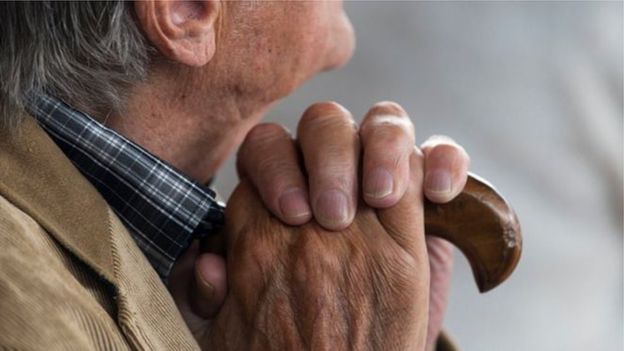 Čovek sede kose drži štap u ruci