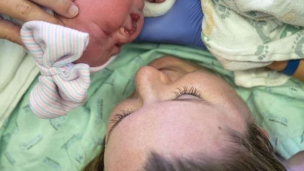 Kayla Edwards sorri, segura e olha para sua filha logo após o parto