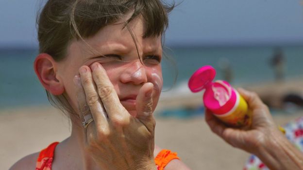 Mujer aplicando crema solar a una niÃ±a.