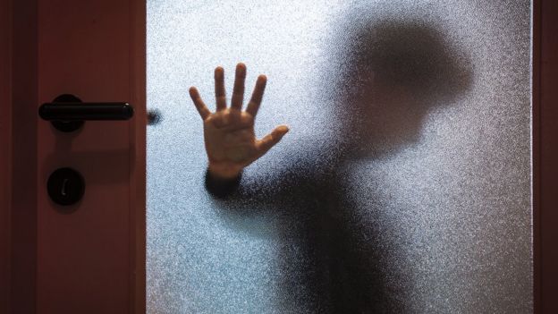 Foto ilustrativa sobre abuso infantil - menino visto através de porta de vidro fosco