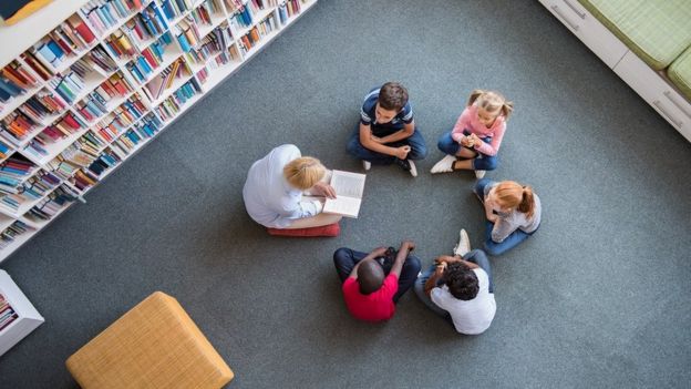 Uma professora lê para um grupo de crianças no chão de uma biblioteca