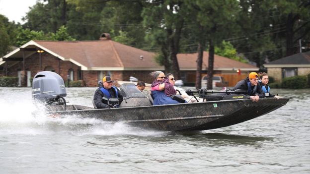 A shallow speedboat moves at high speed through a flooded street in Port Arthur, carrying evacuees