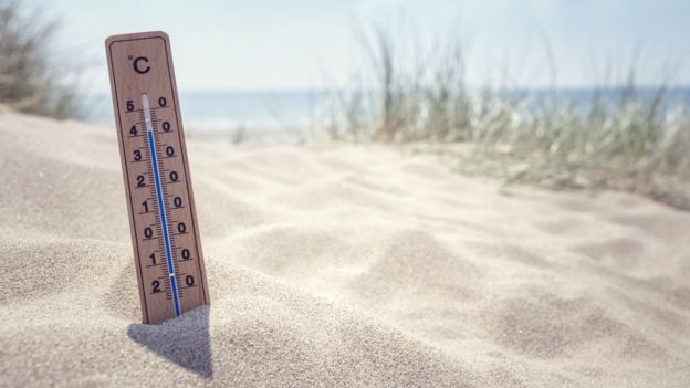 Termômetro fincado em areia de praia marca temperatura alta
