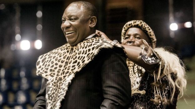 South African President Cyril Ramaphosa (L) smiles as he is adorned with a traditional Zulu attire as a gift from Inkosi (Chief) Mandla Mkwanazi in Empangeni, some 145 kilometres north of Durban, on October 14, 2018, during a ceremony to mark the successful transfer of land and ownership to the community following a land claim