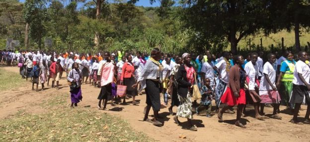 Parents and students form a long line as they walk along a dirt track for their anti-FGM march