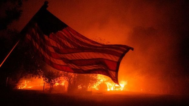 A US flag is seen in the blaze