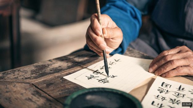 شخص متقدم بالعمر يستخدم أدوات تقليدية من الحبر والفرشاة لكتابة الخط الآسيوي