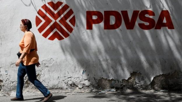 Una mujer camina junto a un cartel de PDVSA en Caracas.