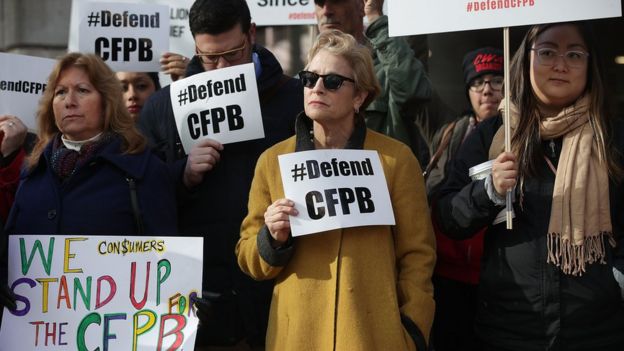 Supporters of the Consumer Financial Protection Bureau hold signs as they gather in front of the agency in Washington DC