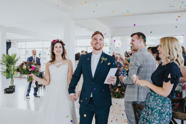 Married couple walk down the aisle as colourful confetti is thrown