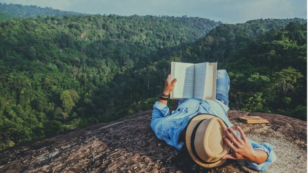 Young man relaxing and reading a book at the top of a rocky cliff, on holiday in Thailand.