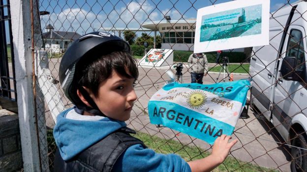 Niño con una bandera argentina y una foto del submarino