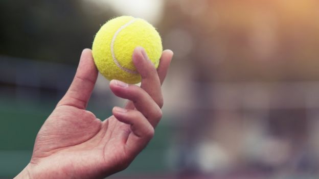 Una mano agarrando una pelota de tenis.