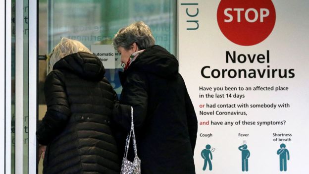 Two women walk past a sign providing guidance information about novel coronavirus (COVID-19)