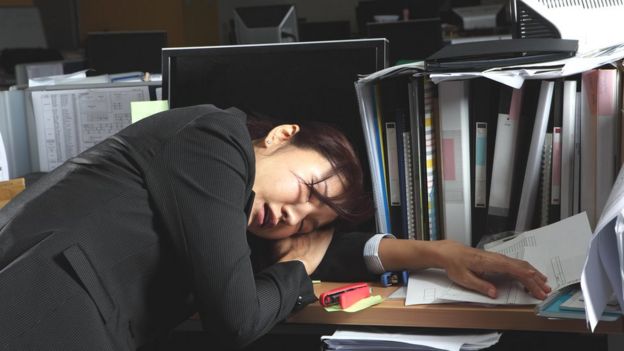 Mujer de rasgos asiáticos dormida sobre el escritorio de la oficina.