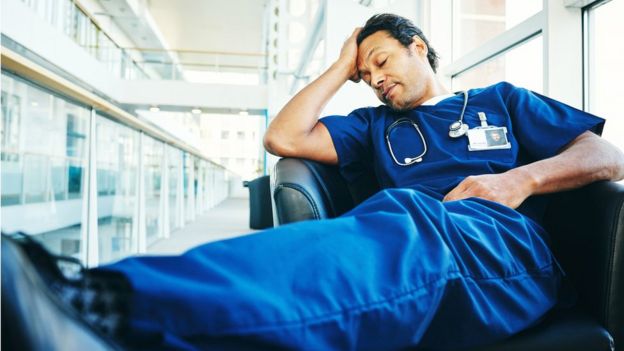 Un médico cansado duerme en un sillón de hospital.