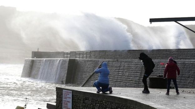 People watch waves crashing against the seafront in Auderville, Normandy, as storm Eleanor hits the northern part of France on 3 January 2018