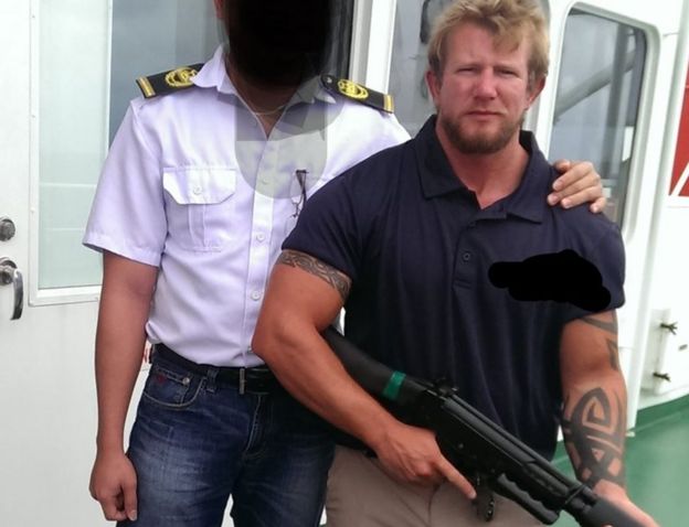 Nick Dunn holds gun next to ship officer