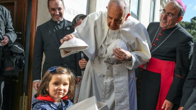 Pope Francis, accompanied by Leiria-Fatima Bishop Antonio Marto (right), changes skull-caps with a young child at the entrance of the Our Lady Rosario Cathedral at the Fatima Sanctuary, in Leiria, Portugal, 13 May 2017