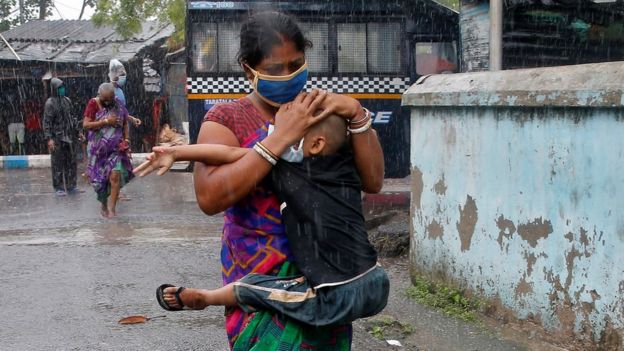 A woman carries her son as she tries to protect him from heavy rain while they rush to a safer place, following their evacuation from a slum area before Cyclone Amphan makes its landfall, in Kolkata