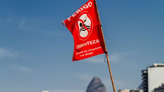 Bandeira vermelha fincada em praia no Rio de Janeiro dizendo: 'Perigo, correnteza - Você pode ser arrastado e se afogar'