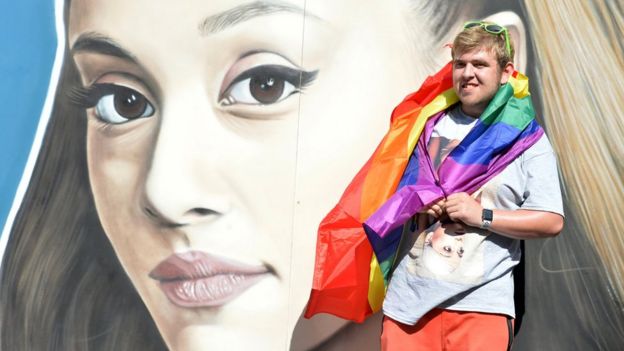 A Pride reveller in front of a mural of Ariana Grande's face in Manchester