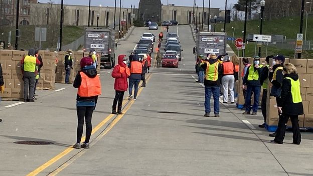 Voluntários com coletes laranja organizam fila de carros que vão receber doação de alimentos