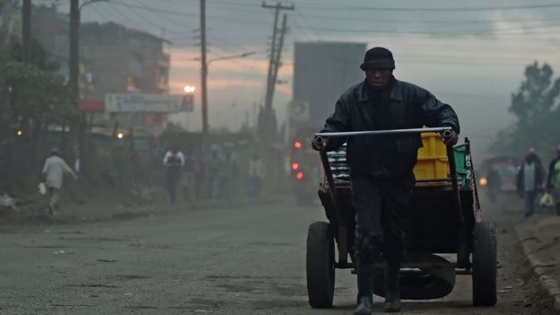 Homem carrega carroça em rua de Nairobi, onde se pode ver o amanhecer sob fumaça