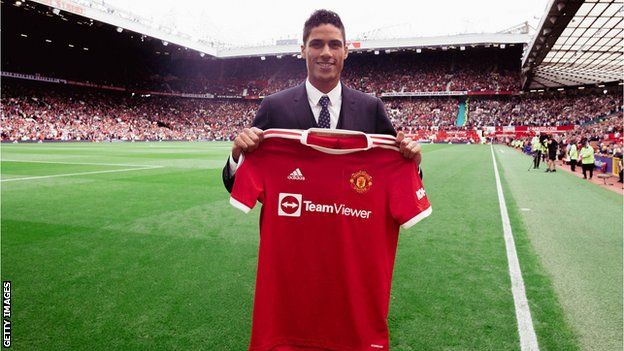Raphael Varane poses on the Old Trafford pitch with his Manchester United shirt