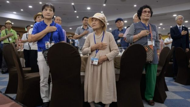 Elderly South Koreans and assistants stand for the national anthem at a briefing in a hotel (19 Aug 2018)