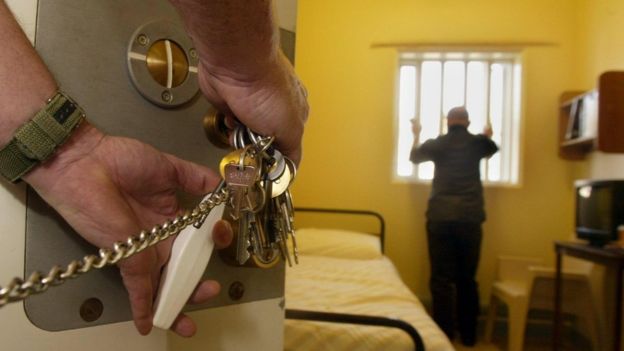 Un détenu non identifié au Royaume-Uni regarde par la fenêtre pendant qu'un gardien de prison l'enferme.