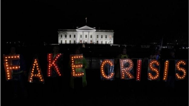 Activists hold a lit 'FAKE CRISIS' sign as they stage a protest outside the White House in response to U.S. President Donald Trump's prime time address
