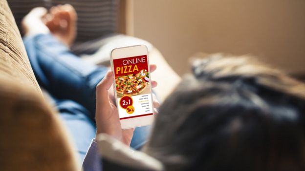 pessoa no sofá pede pizza pelo celular