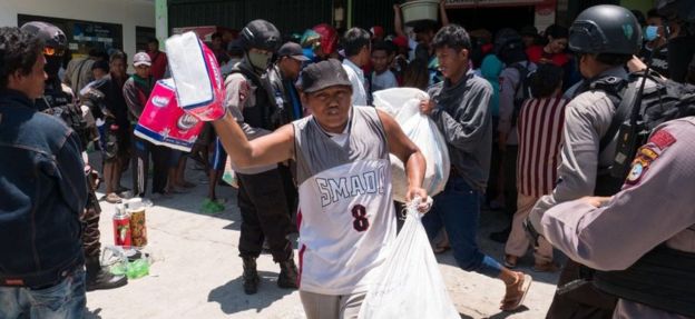 People leave a shop carrying looted goods in Palu