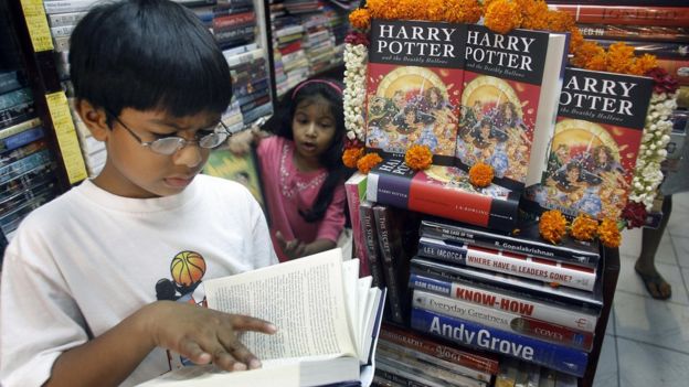 A young Indian boy reads a book next to a stack of Harry Potter books