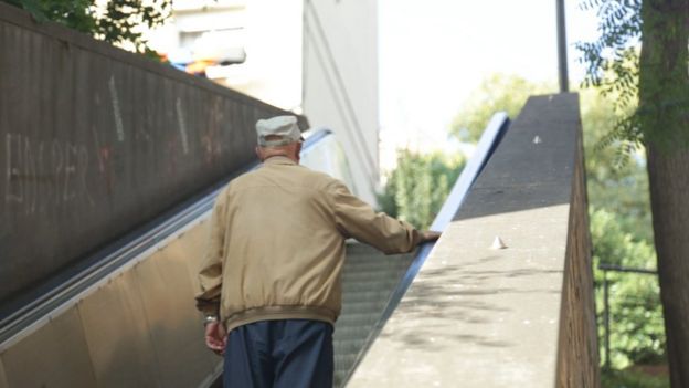 Un hombre anciano sube una escalera mecánica.