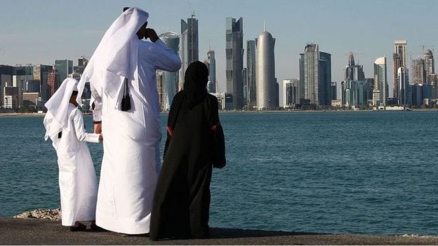 Um homem e duas crianças em trajes tradicionais olham para uma cidade no Golfo Pérsico
