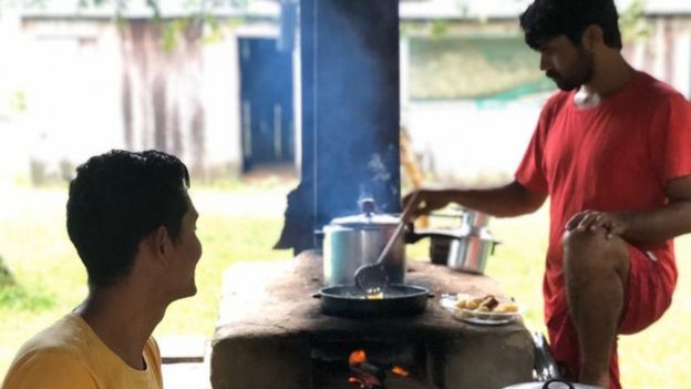 Joelmir e outro homem em cozinha externa com fogão à lenha