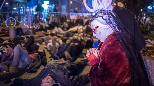 Hombre pintado reza delante de un gruò de personas