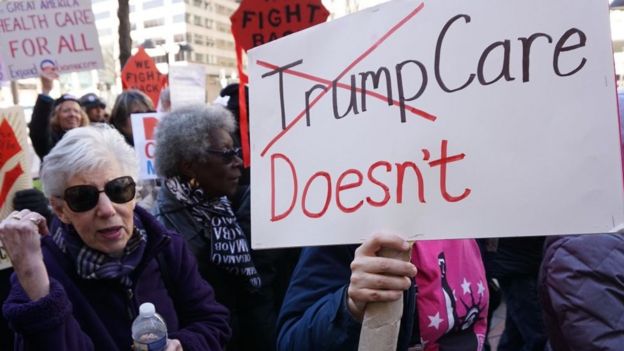 A woman holds a sign criticising Donald Trump's healthcare policies.