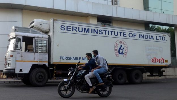 Dois homens em moto passam em frente a caminhão exibindo a inscrição: Serum Institute of India