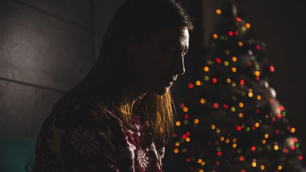 Una mujer sola al lado de un árbol de navidad