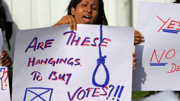 A woman protesting outside Welikada prison on 28 June holds a placard saying "Are these hangings to buy votes?!!"