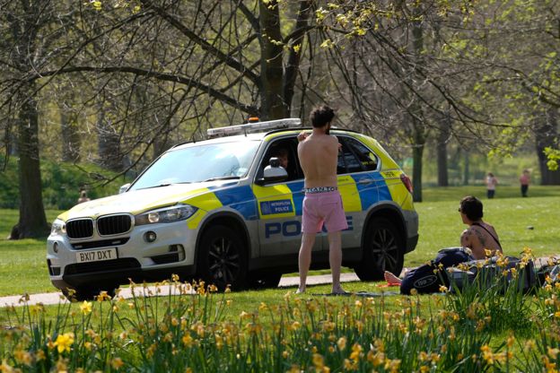 Police officers talk to two men who had been sunbathing in St James's park in central London on Saturday