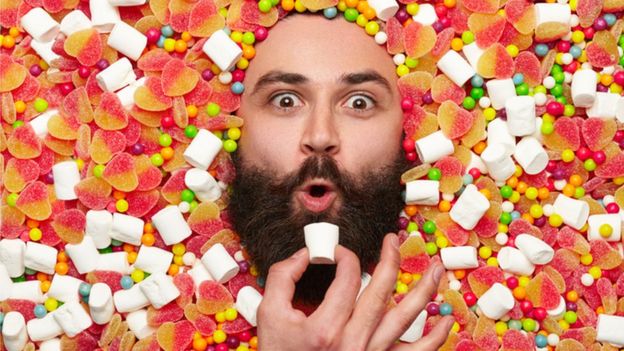 Imagem de rosto de homem rodeado de balas e coisas doces