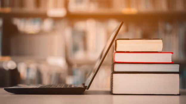 Una laptop junto a varios libros.