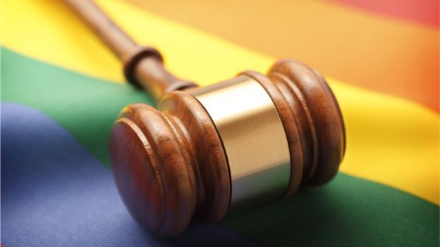 Martelo que representa a Justiça sobre bandeira com cores do arco-íris, representando a comunidade LGBT