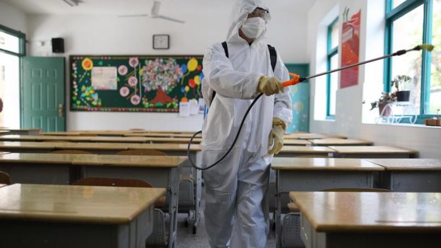 Escola sendo higienizada por homem com uniforme branco de proteção