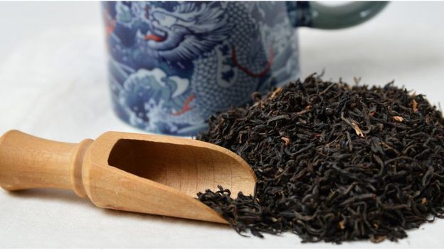 Folhas de chá preto com colher de madeira e cerâmica oriental ao fundo