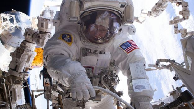 Imagem de astronauta flutuando no espaço, perto de sondas e equipamentos